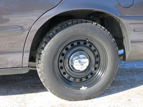 2001 Ford Crown Victoria - The rear wheel and fender of a 2001 Ford Crown Victoria are visible, fitted with a steel rim and a snow tire.