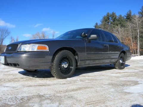 2001 Ford Crown Victoria - A dark gray 2001 Ford Crown Victoria sedan is viewed from a three-quarter front angle on a bright, clear day.