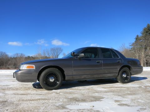 2001 Ford Crown Victoria - A 2001 Ford Crown Victoria sedan is parked on a snowy surface under a bright blue sky.