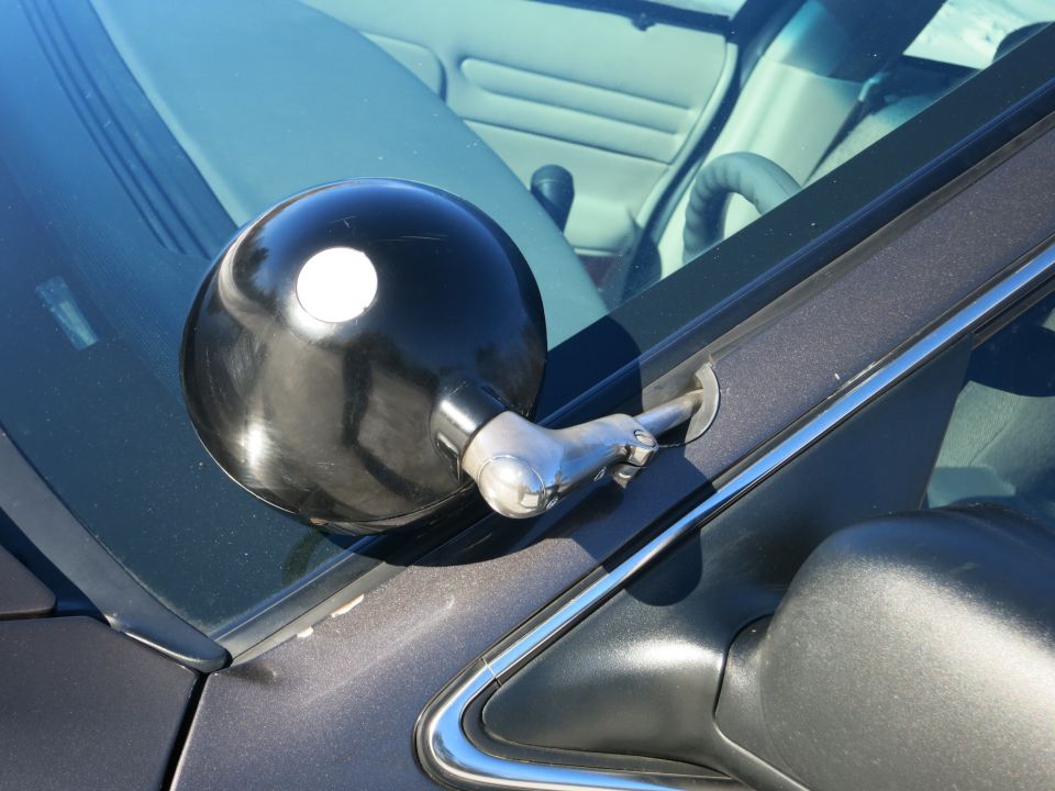 Close-up of a black spotlight mounted on the A-pillar of a car. Interior details like the steering wheel and dashboard are visible