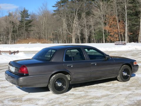 2001 Ford Crown Victoria - A dark grey 2001 Ford Crown Victoria sedan is parked in a snowy area with trees visible behind it.