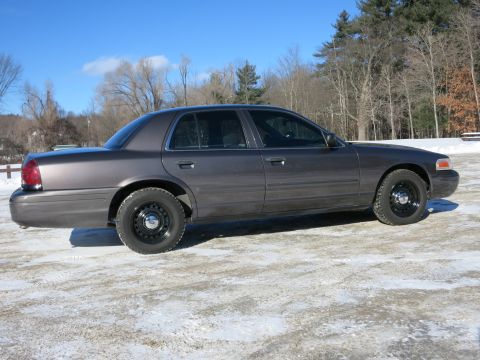 2001 Ford Crown Victoria - A dark gray 2001 Ford Crown Victoria sedan is parked on a snowy surface with trees in the background.