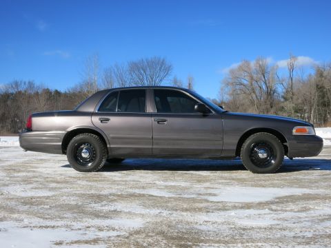 2001 Ford Crown Victoria - Side profile of a gray 2001 Ford Crown Victoria sedan with black steel wheels, captured on a clear winter day.