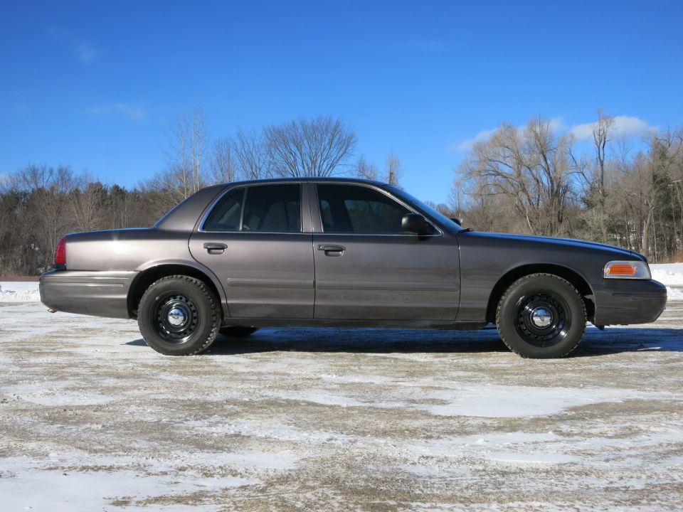 Gray 2001 Ford Crown Victoria sedan, side view, black wheels, parked on snowy ground
