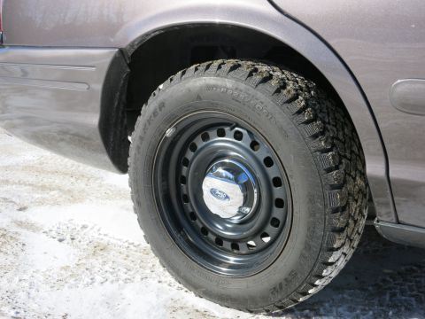 2001 Ford Crown Victoria - The rear wheel and fender of a 2001 Ford Crown Victoria are visible, showing a Ford logo on the hubcap.