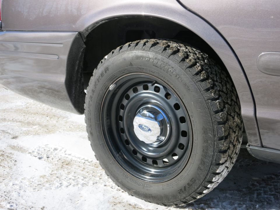 Rear wheel and fender of a 2001 Ford Crown Victoria with a Ford logo on the hubcap