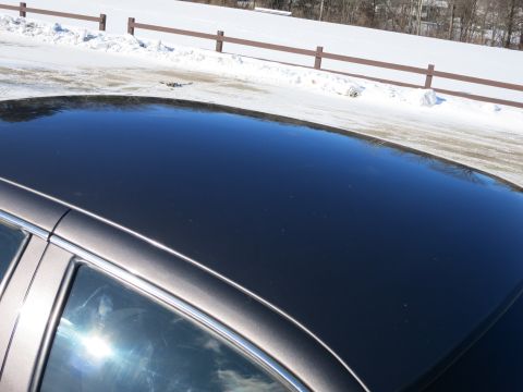 2001 Ford Crown Victoria - The sun reflects off the dark roof of a car parked near a snow-covered area with a wooden fence.