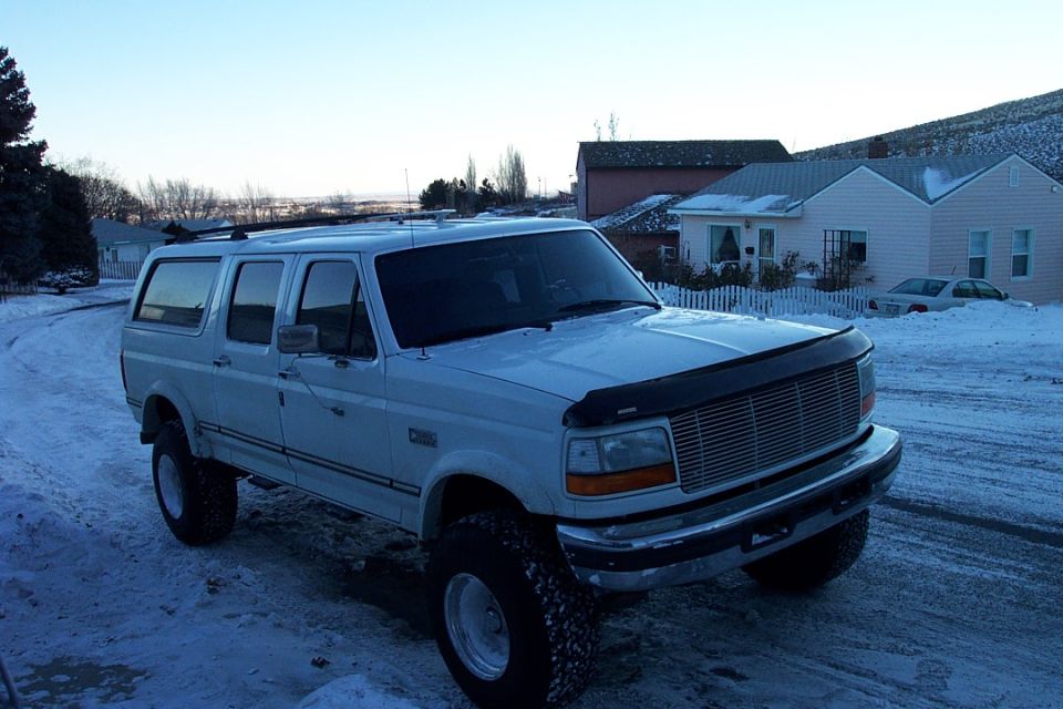 White lifted Ford crew cab with cap parked on a snowy lot beside tan houses