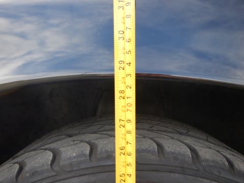 2003 Ford Crown Victoria - yellow tape measure runs vertically from a tire up over a dark fender, marking roughly 31 inches against the sky.