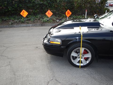 2003 Ford Crown Victoria - black sedan with silver wheels and red brake calipers sits before orange road signs as a tape measure spans its fender.
