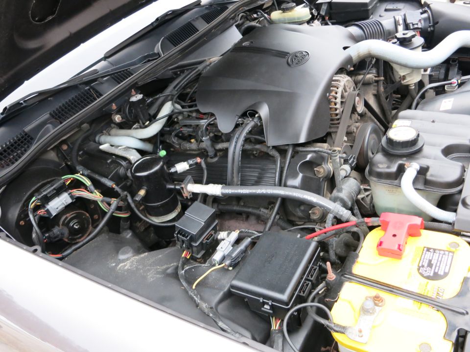 2001 Ford Crown Victoria engine bay with black engine cover and yellow battery