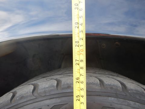 2003 Ford Crown Victoria - yellow tape measure extends vertically from a tire over a dark fender, reading near 30 inches under a cloudy sky.