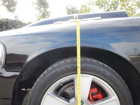2003 Ford Crown Victoria - yellow tape measure is held over the wheel of a black car fitted with an Eagle-brand tire and a red brake caliper.