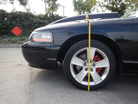 2003 Ford Crown Victoria - yellow tape measure spans the front fender of a black sedan with a silver five-spoke wheel and red brake caliper.