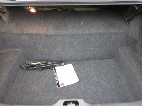 2001 Ford Crown Victoria - The interior of a car trunk shows a scissor jack and a document on the carpeted floor.