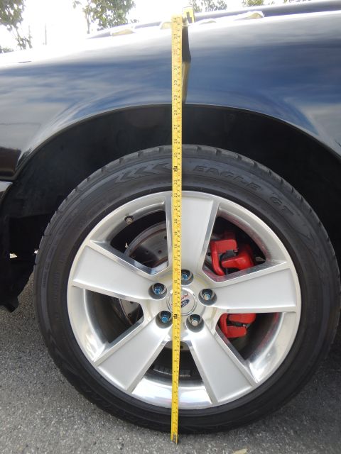 2003 Ford Crown Victoria - yellow tape measure runs vertically next to a silver five-spoke wheel with a red brake caliper on a dark vehicle.