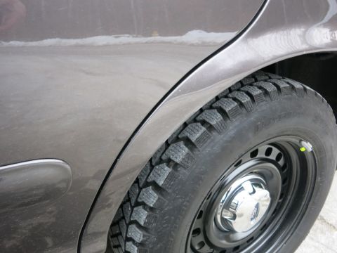2001 Ford Crown Victoria - Close-up of a dark gray sedan's rear wheel and fender, showing a snow tire on a steel rim.