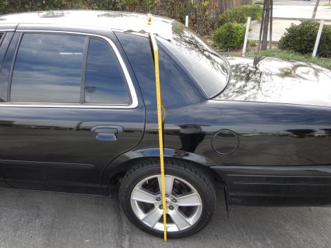 2003 Ford Crown Victoria - yellow tape measure is held vertically at the rear quarter panel of a black sedan with a silver wheel.