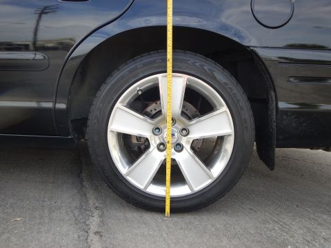 2003 Ford Crown Victoria - yellow tape measure runs down beside the front wheel of a dark car fitted with a silver seven-spoke wheel.