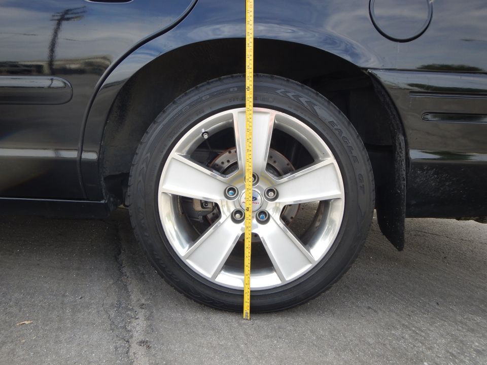 Front wheel of a dark car with silver seven-spoke wheel and tape measure