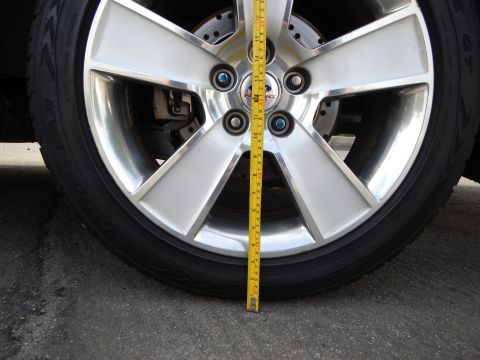 2003 Ford Crown Victoria - Close-up of a polished five-spoke alloy wheel with a Ford center cap, low-profile tire, and a tape measure laid across the wheel face.