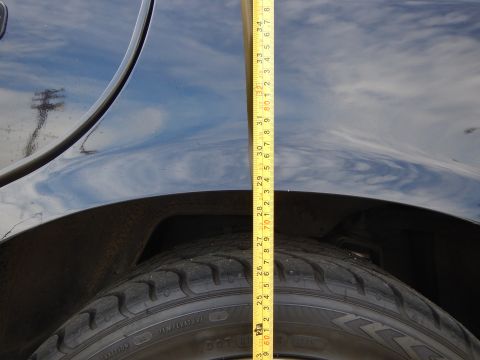 2003 Ford Crown Victoria - Vertical tape measure spanning a glossy dark fender down to the tire, with sky reflected in the paint, measuring ride height.