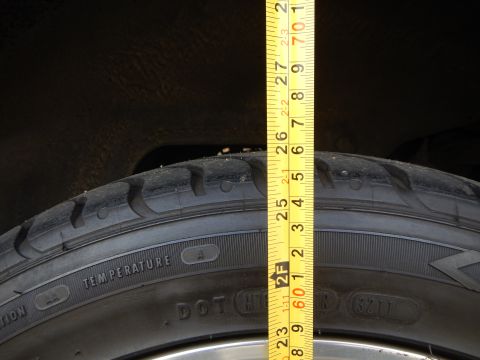 2003 Ford Crown Victoria - Close-up of a tire tread and sidewall showing DOT markings, with a tape measure held vertically against the dark wheel well.