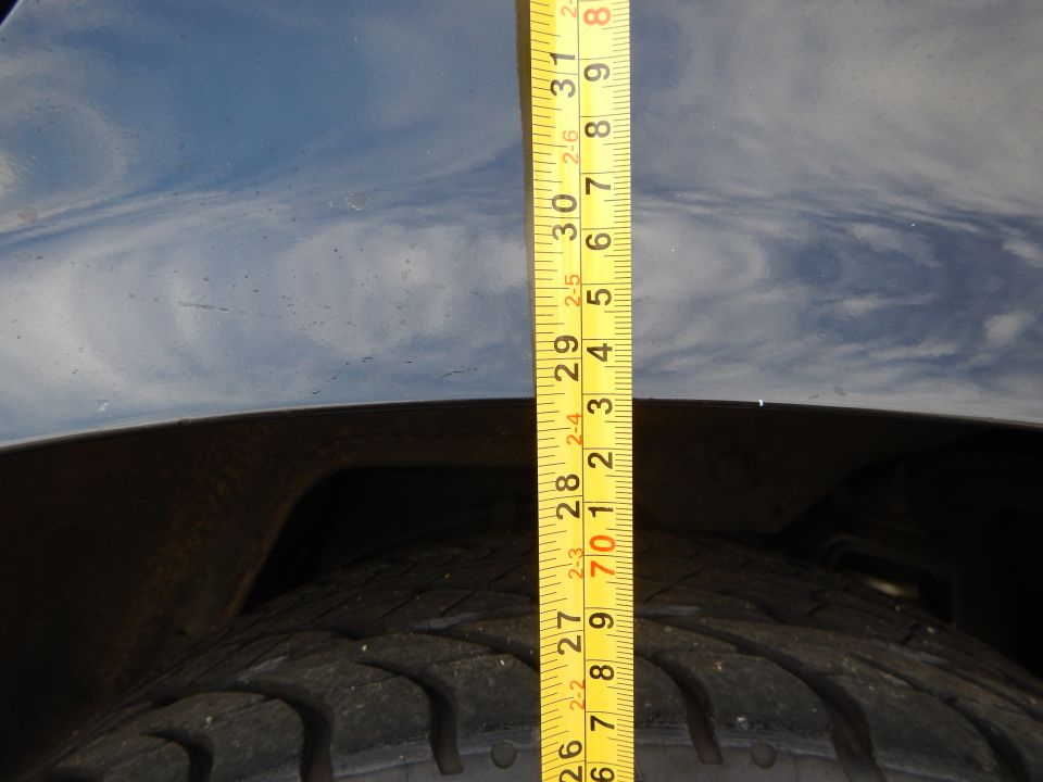 Dark fender arch and tire with vertical tape measure against sky