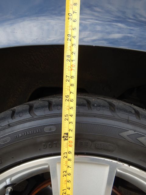2003 Ford Crown Victoria - tape measure runs down a dark wheel well across a tire sidewall with temperature and DOT markings to a silver wheel.
