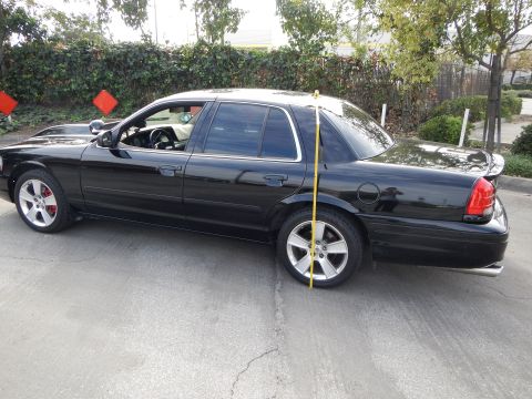 2003 Ford Crown Victoria - Side profile of a black four-door sedan with silver alloy wheels and red brake calipers, a tape measure standing at the rear wheel.