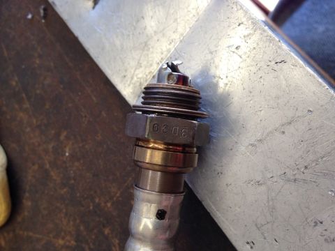 2010 Dodge Challenger - Close-up of an oxygen sensor, identified by the stamped '0308' on its hex nut, resting against a metallic surface.