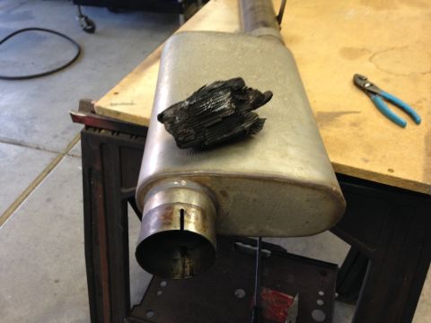 2010 Dodge Challenger - A damaged muffler sits on a workbench with a piece of burnt debris and a pair of pliers nearby.