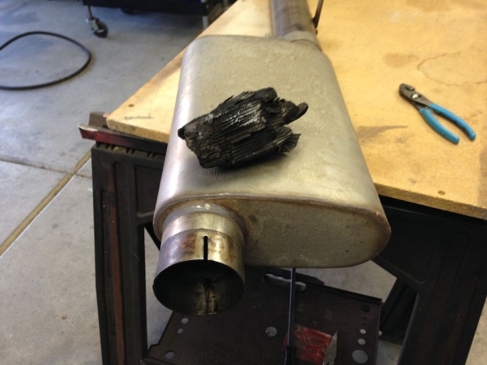 Muffler with a chunk of burnt material on top, next to pliers