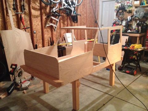 2005 Jeep Wrangler - A partially constructed wooden vehicle body sits on sawhorses in a workshop, surrounded by tools and bicycles.