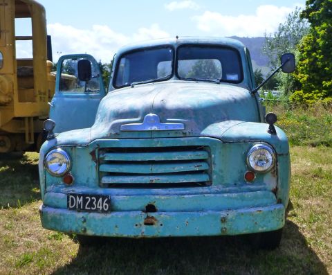 1969 Lincoln Continental - This old blue truck sits in a grassy field next to a yellow piece of heavy machinery.