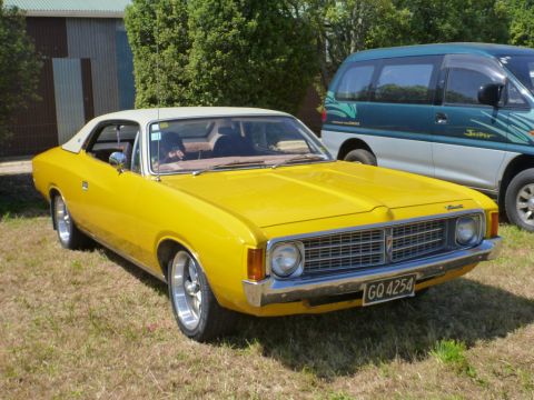 1969 Lincoln Continental - A yellow coupe with a white roof is parked on grass next to a van. The car has a chrome grille and bumper.
