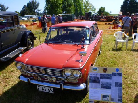 1969 Lincoln Continental - A red Fiat 65 is displayed at an outdoor event, with other vehicles and people in the background.