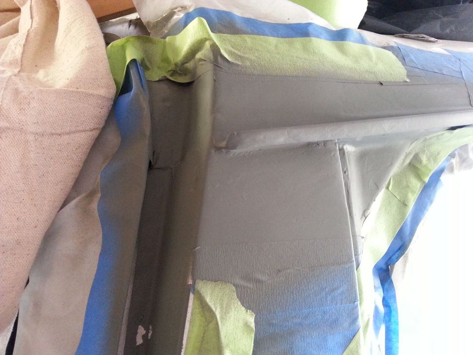 Gray automotive body panel covered in blue and green masking tape, with a tan cloth on the left