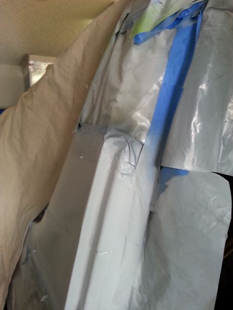 1992 Ford Bronco - A vehicle body panel is covered in masking tape and plastic sheeting, indicating preparation for painting.