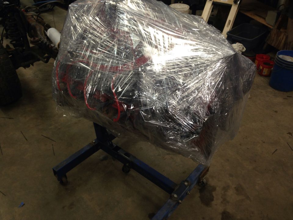 Engine wrapped in plastic on a blue engine stand in a garage