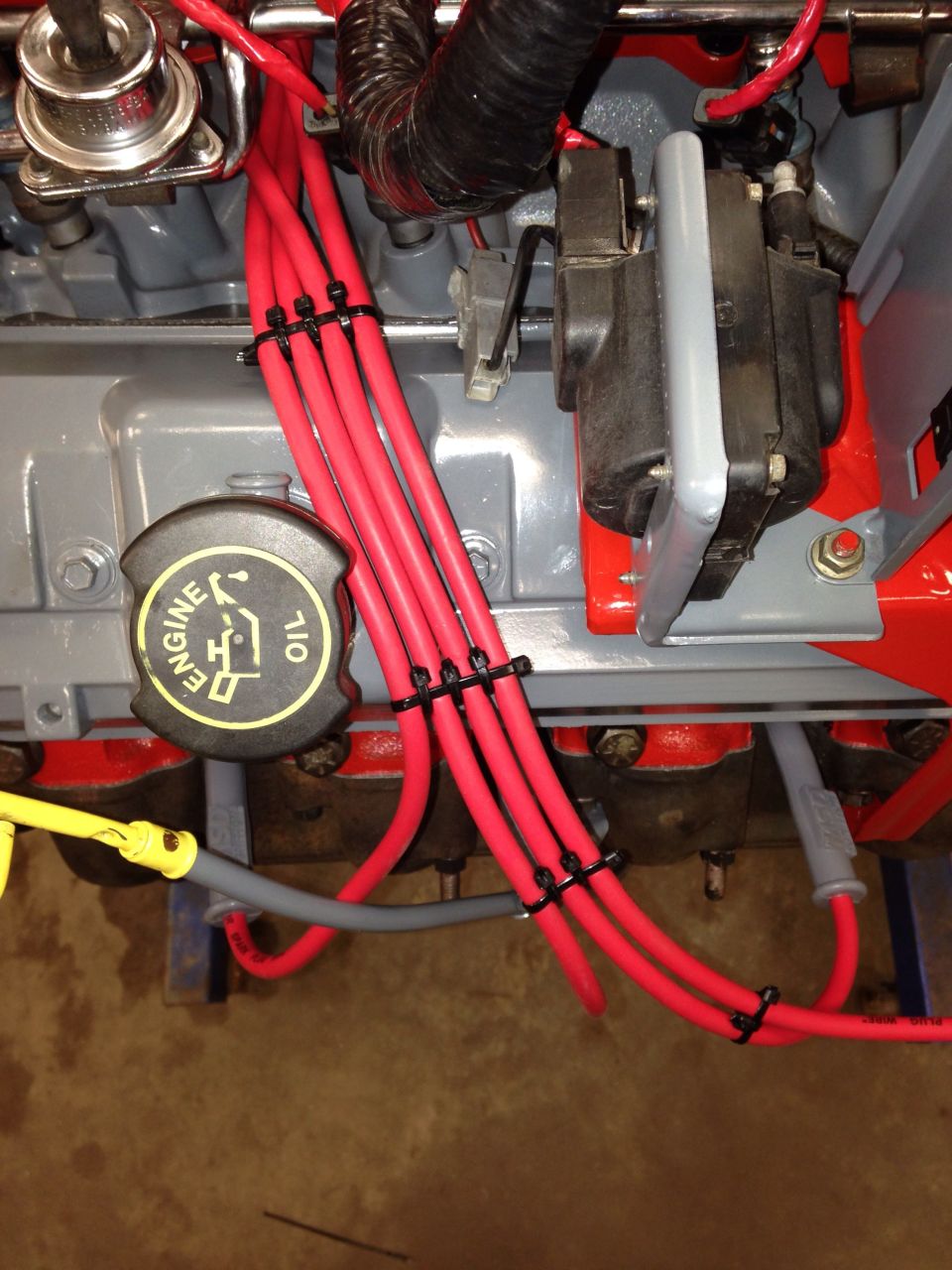 Engine bay detail showing red spark plug wires, ignition coil, and black engine oil cap