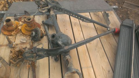 1986 Ford Bronco - Various front axle and suspension components are laid out on a wooden surface, with some rust visible.
