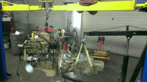1996 Ford Bronco - An engine and transmission assembly is being lifted by an engine hoist in a workshop.
