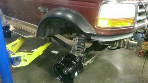 1996 Ford Bronco - Maroon Ford Bronco front fender and suspension visible on a lift, with a detached wheel on the ground.
