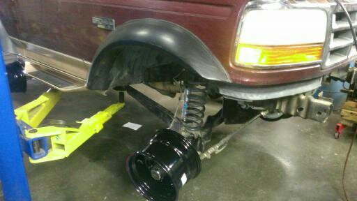 Maroon Ford Bronco front fender and suspension on a lift, with a detached wheel