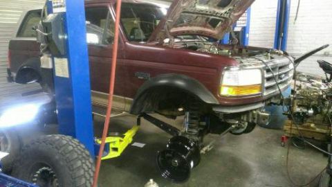 1996 Ford Bronco - A maroon 1996 Ford Bronco is shown on a lift with its hood open, undergoing service in a garage.