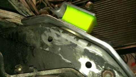 1996 Ford Bronco - Close-up of a yellow engine mount attached to a metal bracket, with a radiator visible in the background.
