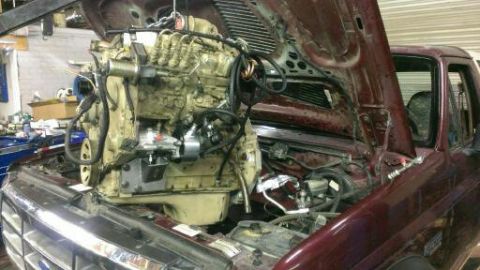1996 Ford Bronco - A large engine is being installed into the engine bay of a maroon truck.