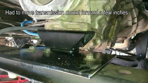 Underside of a vehicle showing a modified transmission mount with bolts and metal plates