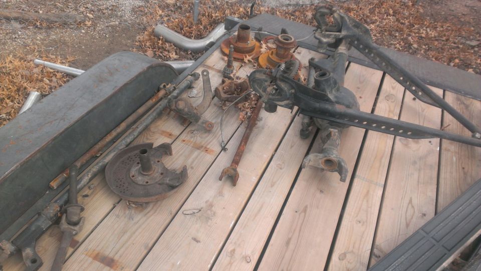 Trailer loaded with various rusty vehicle suspension components, including axles and steering parts